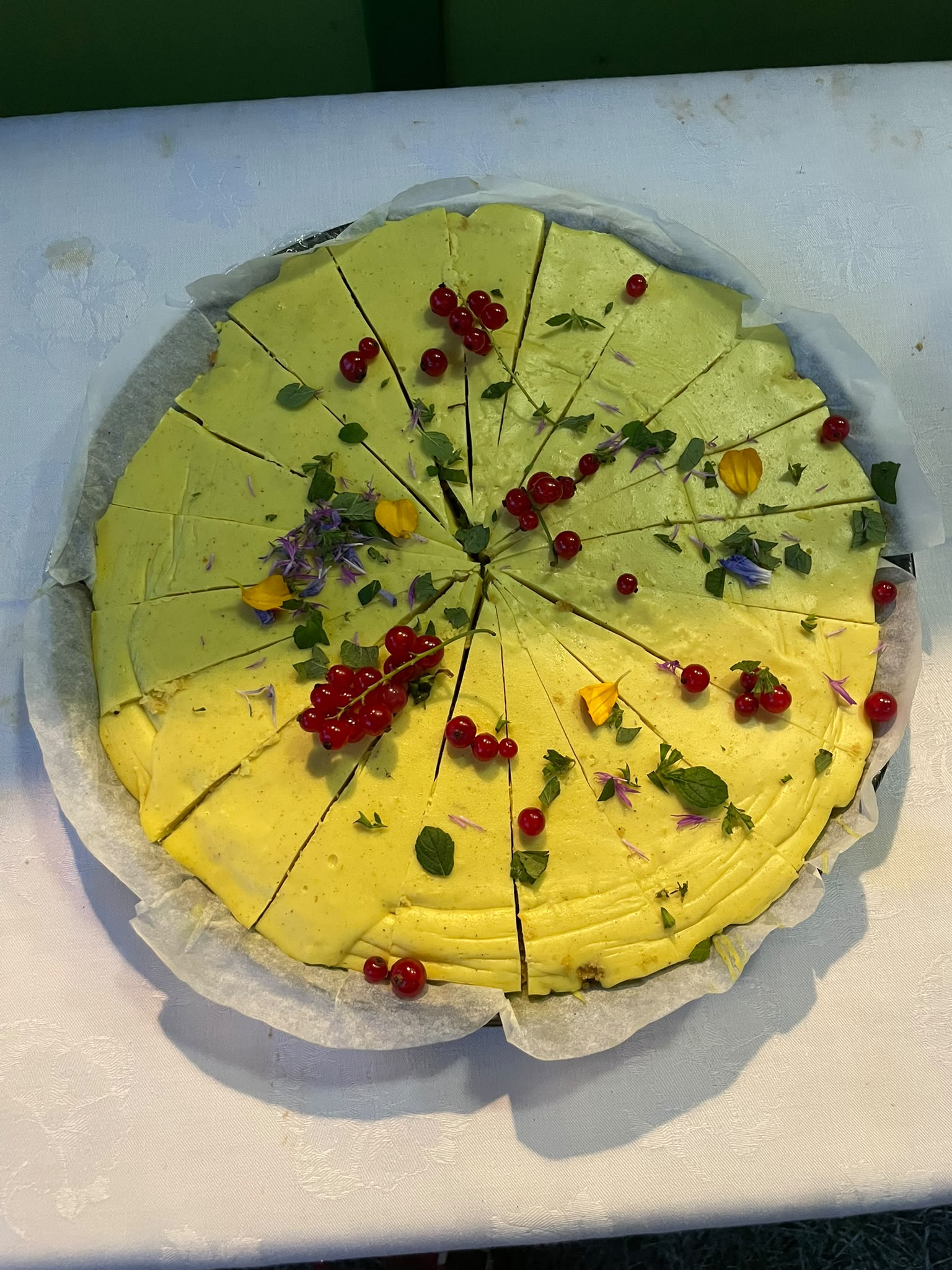Runde Zitronentarte, in Stücke geschnitten, mit Johannisbeeren und Blüten dekoriert