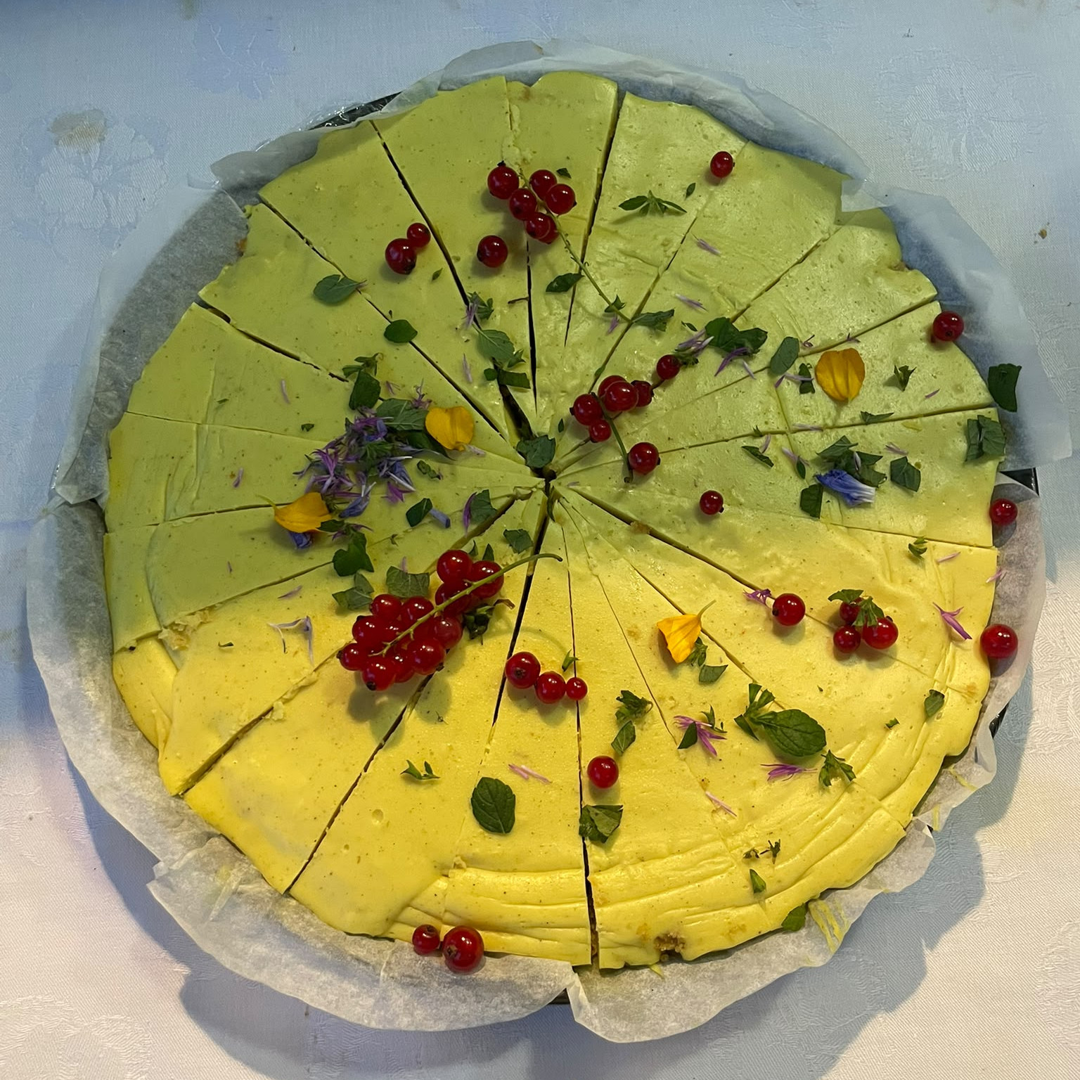 Round lemon tart, cut into pieces, garnished with redcurrants and edible flowers